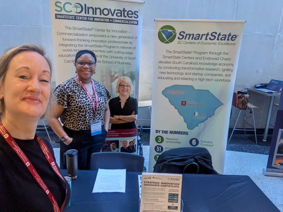 2 women standing by a table and in front of tall banners.